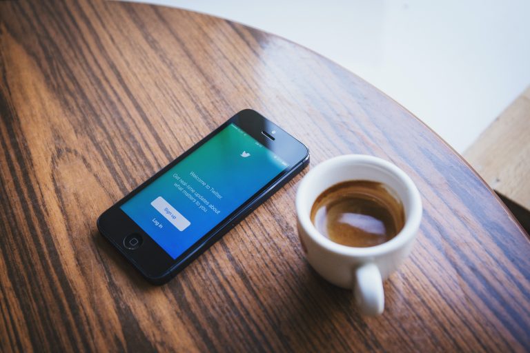 iPhone with Twitter on the screen, sitting on a table net to a mug of coffee